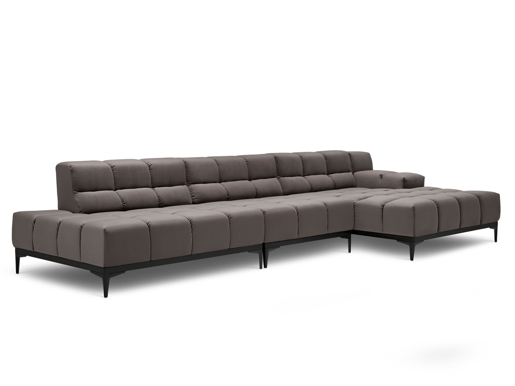 Ein langes L-förmiges Sofa in einem dunklen Taupe-Ton mit gesteppter Sitzfläche und Rückenlehne. Es steht auf schlanken schwarzen Metallfüßen. Es sind keine Zierkissen zu sehen. Der Hintergrund ist weiß.