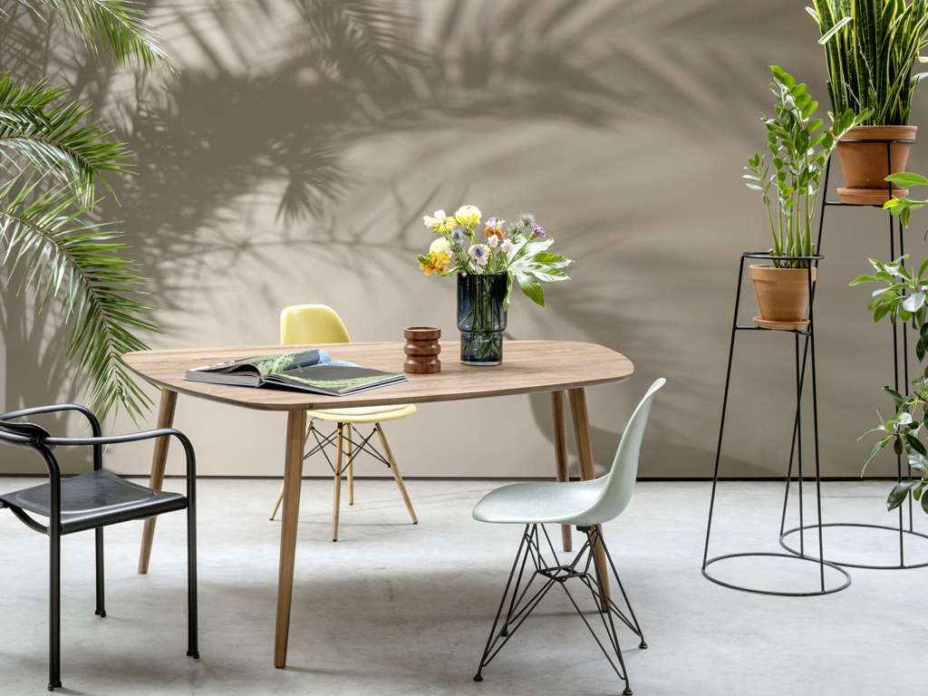 Sudbrock Mellini - Esstisch organisch | B: 170 cm | Nussbaum massiv Essbereich mit ovalem Holztisch, buntem Blumenstrauß, Stühlen und umrahmt von grünen Pflanzen auf Betonboden.
