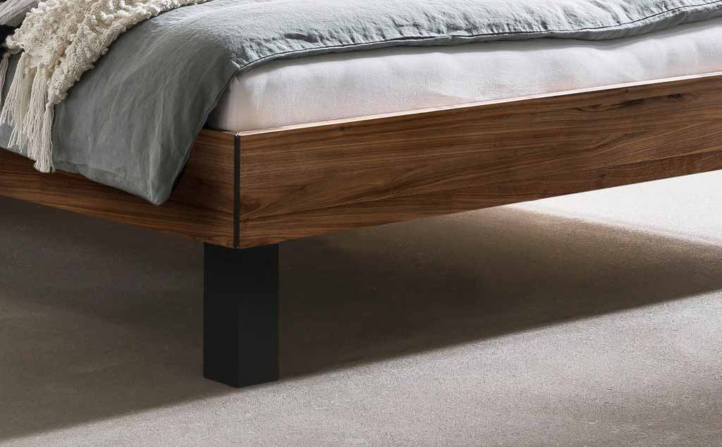 Nahaufnahme eines modernen Bettgestells aus Holz mit dunklen Metallbeinen, graue Bettwäsche
