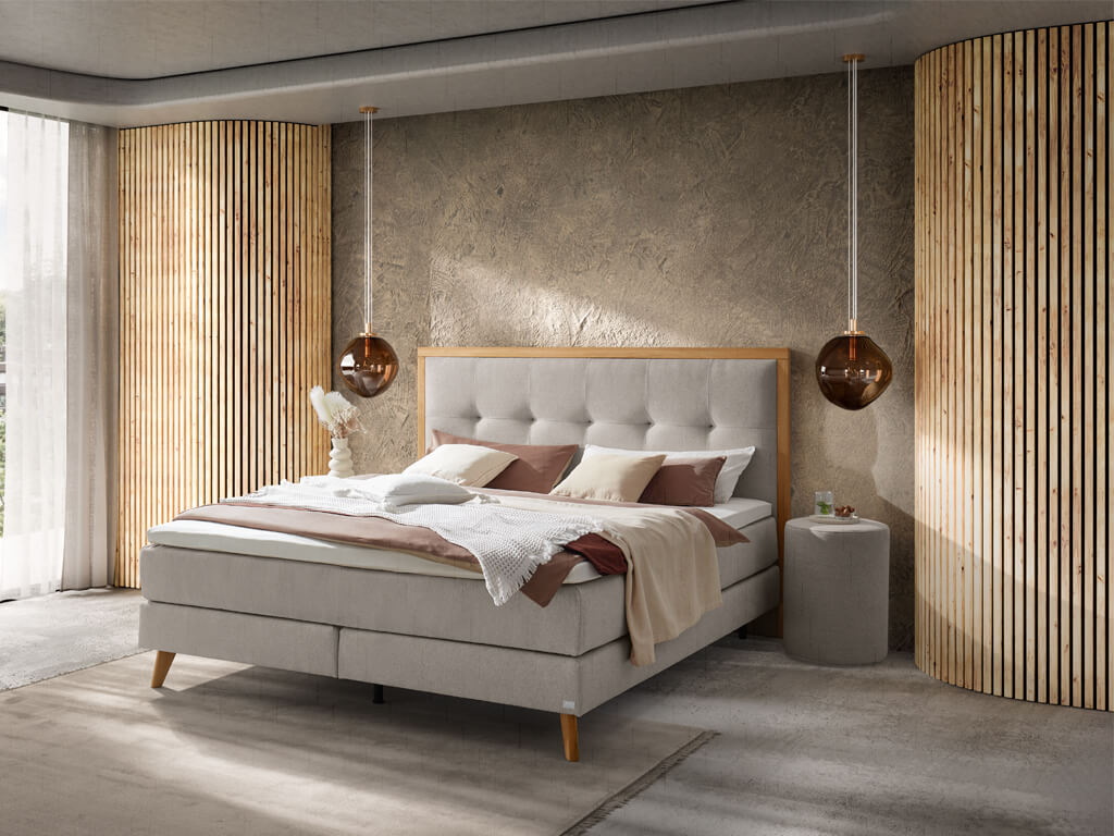 Ein modern gestaltetes Schlafzimmer mit einem hellgrauen Boxspringbett, das von Holzlatten an der Wand und hängenden Leuchten eingerahmt wird.