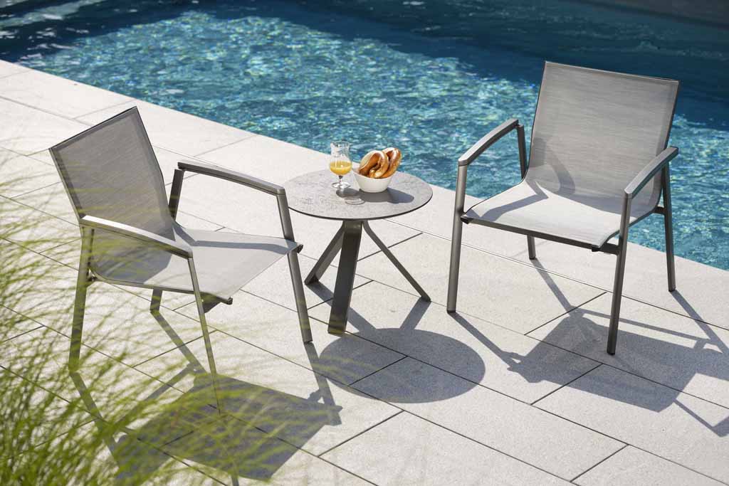 Zwei Stern Gartenstühle und Beistelltisch vor blau strahlendem Outdoopool. 