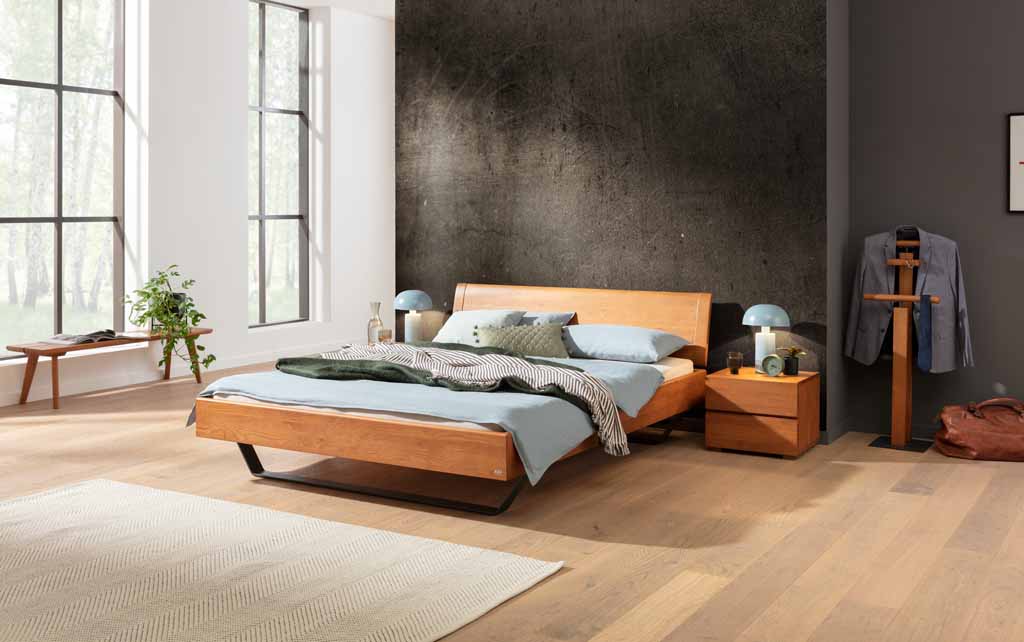Hasena Wood-Line Bett | Eiche brandy, geölt Gemütliches Schlafzimmer mit modernem Holz-Doppelbett, Beistelltisch und großen Fenstern, die viel Tageslicht hereinlassen