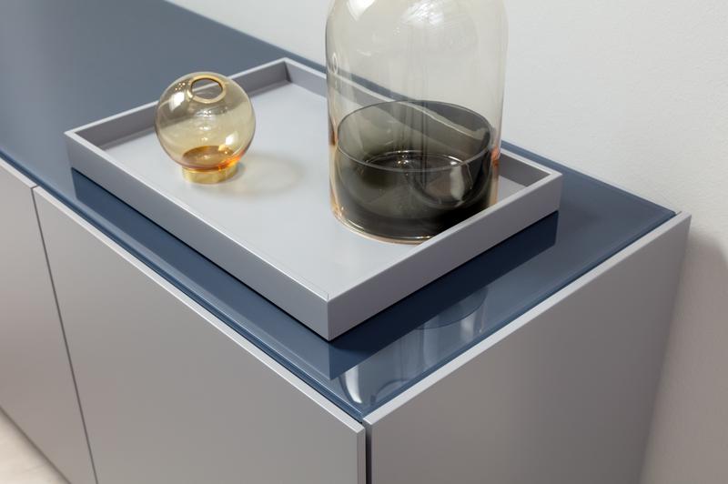 Zwei Glasvasen, eine bernsteinfarbene und eine rauchgraue, stehen dekorativ auf einem modernen, glänzend grauen Sideboard.