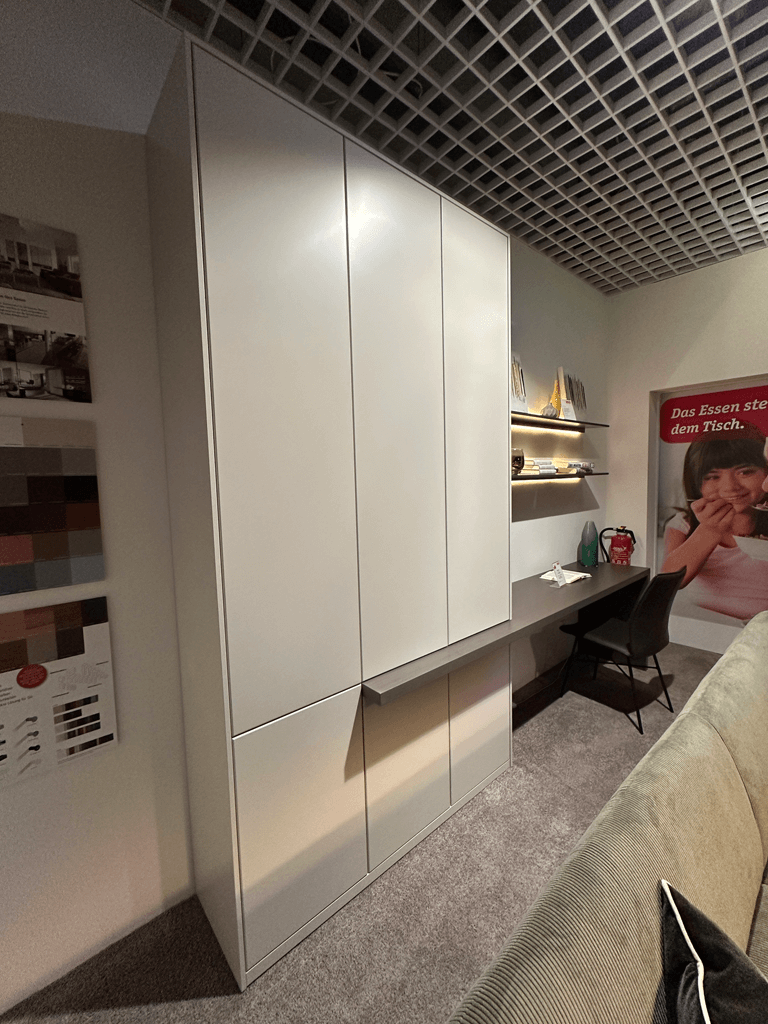 RMW DEVISO | Wohnwand Ein moderner Einbauschrank mit integrierten Regalen und einem Schreibtisch in einem elegant eingerichteten Raum mit Teppichboden und dekorativem Gitter an der Decke.