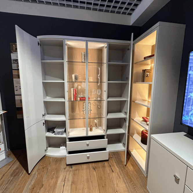 Großer weißer Schrank mit offenen Türen, Glasvitrine und beleuchteten Regalen auf Holzboden