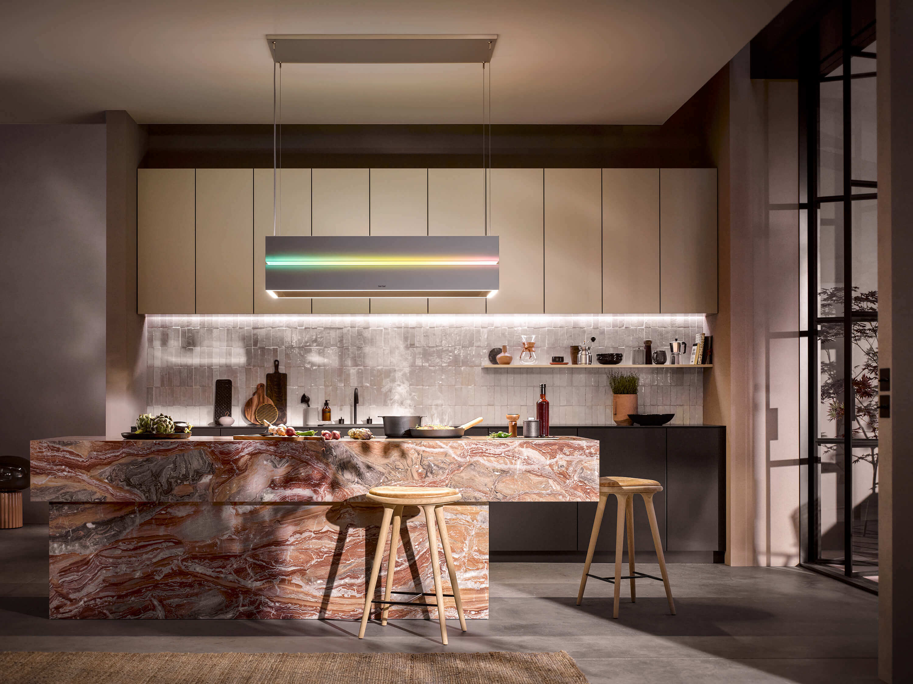 berbel - Skyline Edge Play BIH SKE-P Designerküche mit auffälliger Marmor Kochinsel und Stein-Küchenrückwand und silberner Dunstabzugshaube mit farbigem Lichtstreifen.