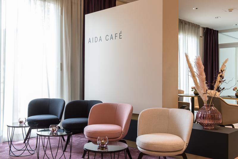 Innenansicht des AIDA Cafés mit stilvollen Sesseln in verschiedenen Farben, kleinen runden Tischen und einer eleganten Blumendekoration