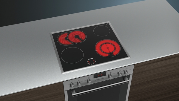 Glaskeramik-Kochfeld mit zwei leuchtenden Kochzonen, integriert in eine Arbeitsplatte aus Edelstahl, mit Bedienelementen und Backofen.