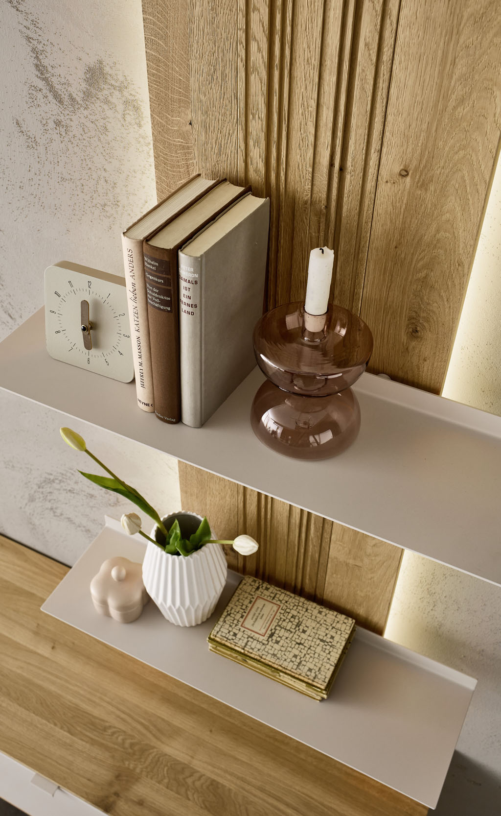 Detailaufnahme eines modernen Wandbords mit markantem Holzpaneel als Rückwand und zwei weißen Ablagen stilvoll dekoriert