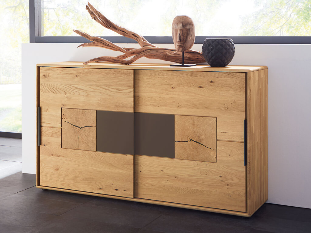 Wöstmann WSM 1600 - Kommode mit Schiebetüren (2167) | Wildeiche massiv Ein eleganter Holzschrank mit einzigartigem Design, dekoriert mit einer Holzskulptur und einer dunklen Vase auf der Oberseite.