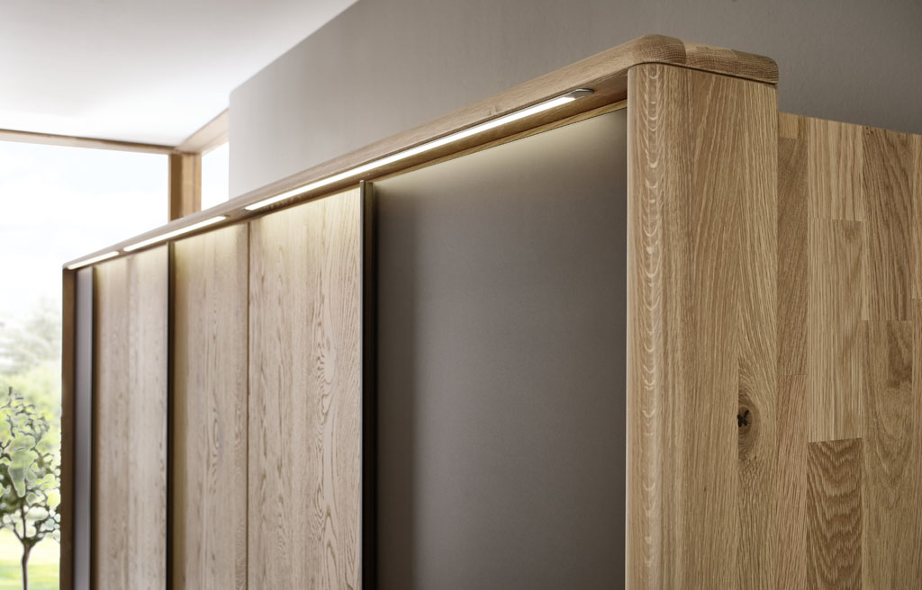 Detailaufnahme eines braunen Holz Kleiderschrankes mit beiden Außentüren in mattem braun und Beleuchtung im Passepartout