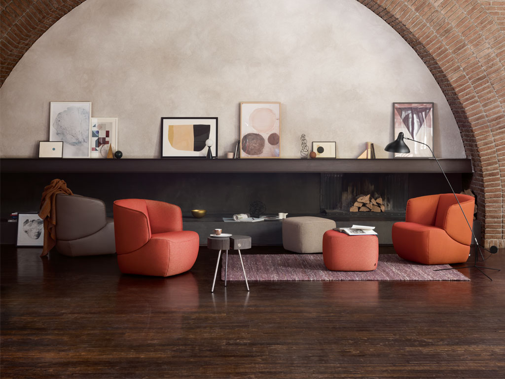 Ein stilvoll eingerichtetes Wohnzimmer mit modernen, orangefarbenen Sesseln, einem flachen Couchtisch und dekorativen Bildern auf einem Regal vor einem Kamin.