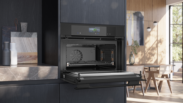 Geöffneter Siemens Kompaktbackofen mit Mikrowelle in einer dunklen Küchenzeile; ein Backblech ist auf den Schienen eingeschoben, das digitale TFT-Display ist aktiv.