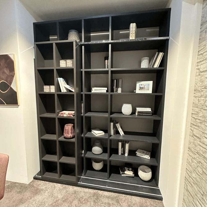 Ein schwarzes Bücherregal mit verschiedenen Büchern und dekorativen Gegenständen in einem modernen Raum.