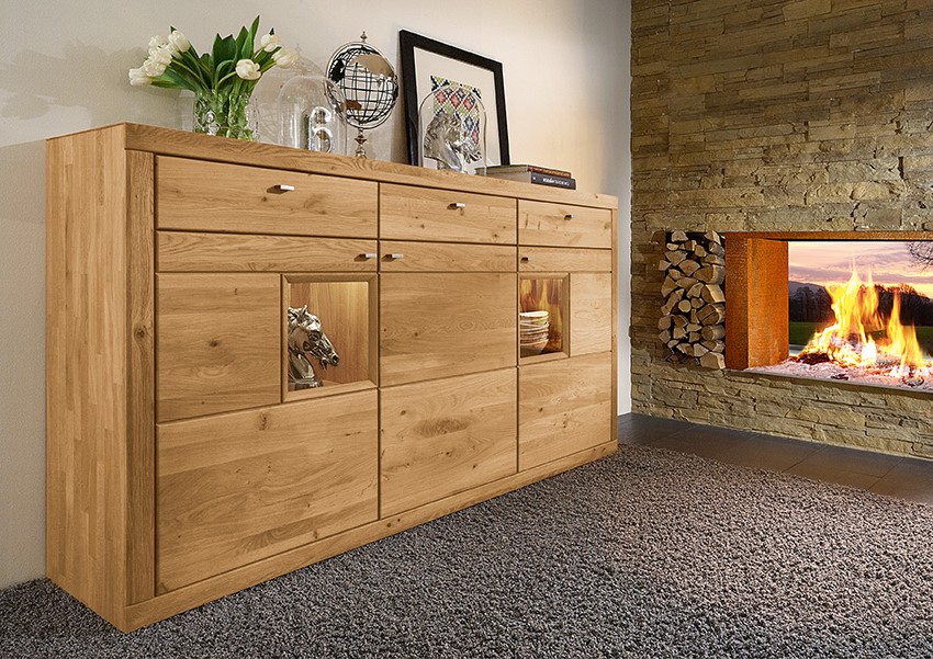 Elegante Holzkommode im Wohnzimmer, dekoriert mit Blumen und Kunst, neben einem Kamin mit brennendem Feuer