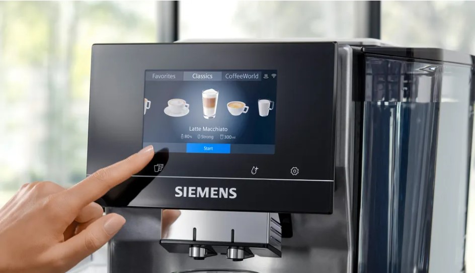 Finger zeigt auf das Touchscreen-Display eines Siemens Kaffeevollautomaten, das Auswahlmöglichkeiten für verschiedene Kaffeespezialitäten anzeigt.