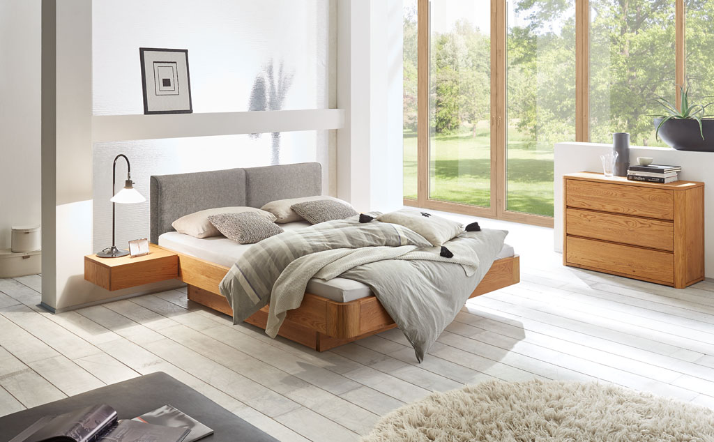 braunes modernes Bett mit braunem Bettkasten und Hängenachtschrank mit grauem Polsterkopfteil und passender brauner Kommode mit drei Schubladen stilvoll dekoriert in einem modernen Zimmer