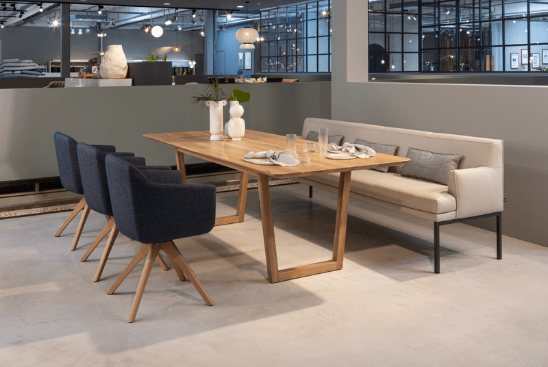 Stilvoll eingerichteter Essbereich mit einem eleganten Holztisch, blauen Polsterstühlen und einer weißen Sitzbank in einem modernen Raum.