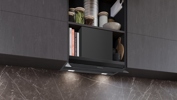 Dunstabzugshaube mit Dekorationsgegenständen im Oberschrank: Eingebaute Siemens studioLine Dunstabzugshaube, der sichtbare Schacht im Oberschrank ist von Kochbüchern, Gewürzgläsern und anderen Küchenutensilien umgeben.