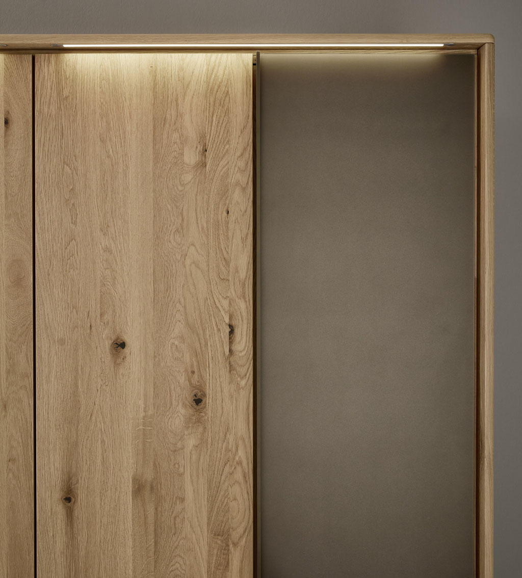 Detailaufnahme eines braunen Holz Kleiderschrankes mit Außentüren in mattem braun und Beleuchtung im Passepartout