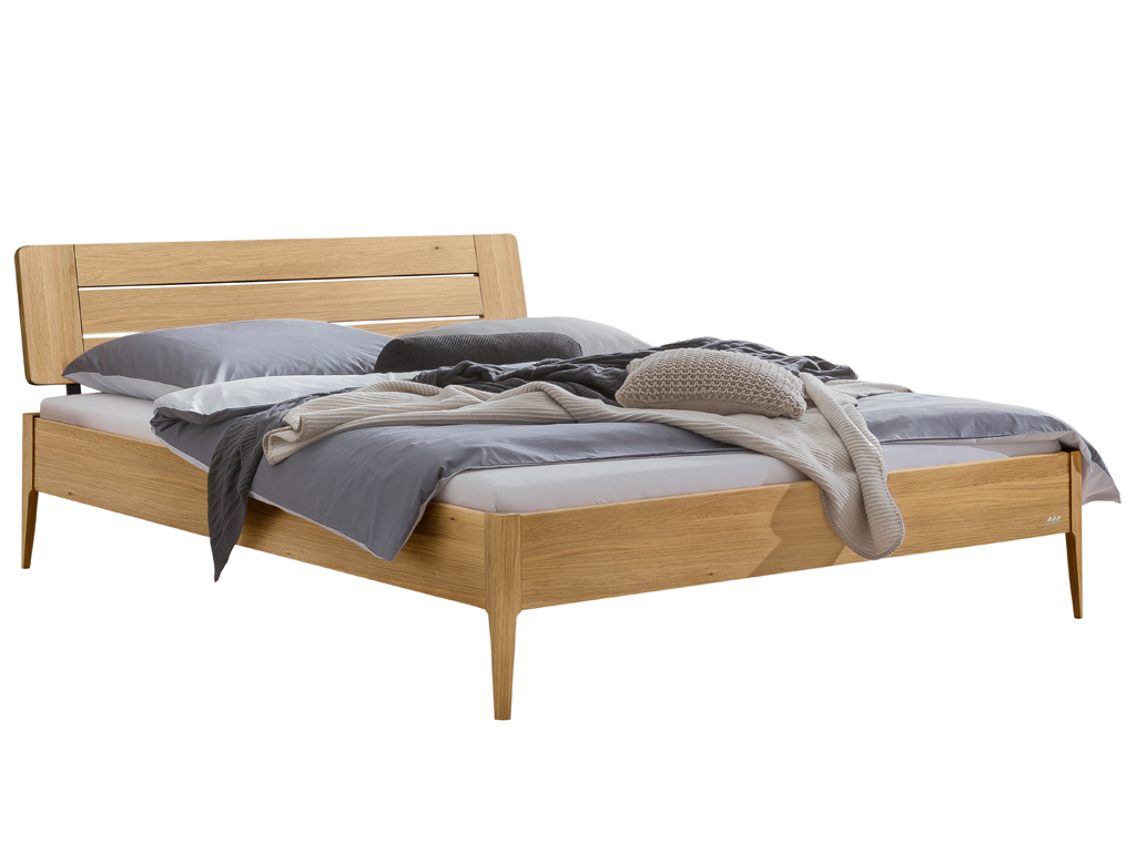 Eine Freisteller-Ansicht des Bettes "Busseto" mit einem Rahmen aus heller Eiche. Das Bett hat ein passendes Holzkopfteil mit horizontalen Lamellen und steht auf vier konischen Holzfüßen. Es ist mit grauer und grüner Bettwäsche dekoriert.