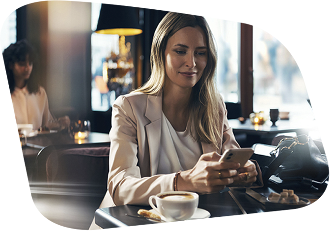 Frau sitzt in einem Café mit Kaffee und bedient ein Smartphone