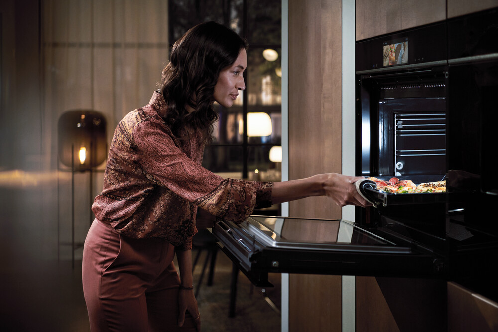 Eine Frau in einer stilvollen Küche legt eine Pizza in einen modernen Einbau-Backofen.