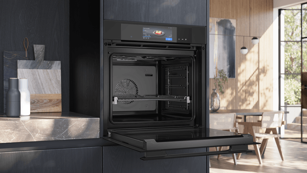Geöffneter Siemens iQ700 Dampfbackofen in der Seitenansicht. Die Backofentür ist vollständig ausgeklappt und gibt den Blick auf den Garraum mit Teleskopauszug und das digitale Bedienmenü frei.