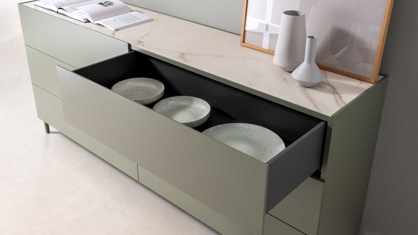 Eine moderne Anrichte mit marmorierter Platte, offenen Schubladen und Geschirr. Oben Dekoration und Bücher.