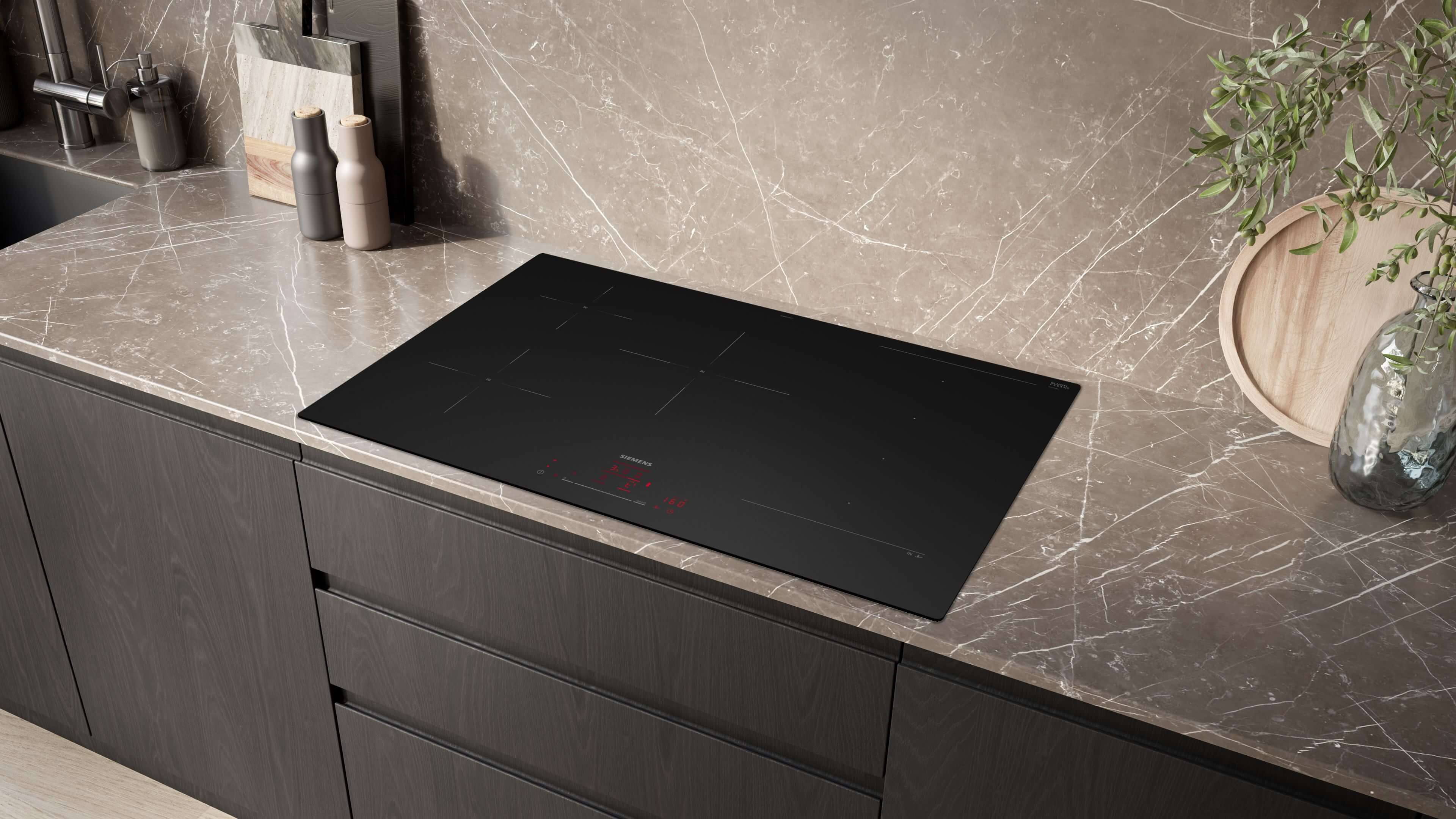 Schrägansicht eines eleganten, schwarzen Siemens-Induktionskochfelds, das in eine moderne Arbeitsplatte mit Marmoroptik eingelassen ist.