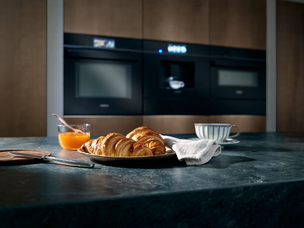  Das Bild zeigt einen Frühstückstisch mit einem köstlichen Gebäck und einer Tasse Kaffee.  Im Vordergrund liegt eine kleine Platte mit zwei goldbraunen Croissants, die frisch und knusprig aussehen.