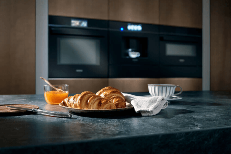 Das Bild zeigt einen Frühstückstisch mit einem köstlichen Gebäck und einer Tasse Kaffee.  Im Vordergrund liegt eine kleine Platte mit zwei goldbraunen Croissants, die frisch und knusprig aussehen.