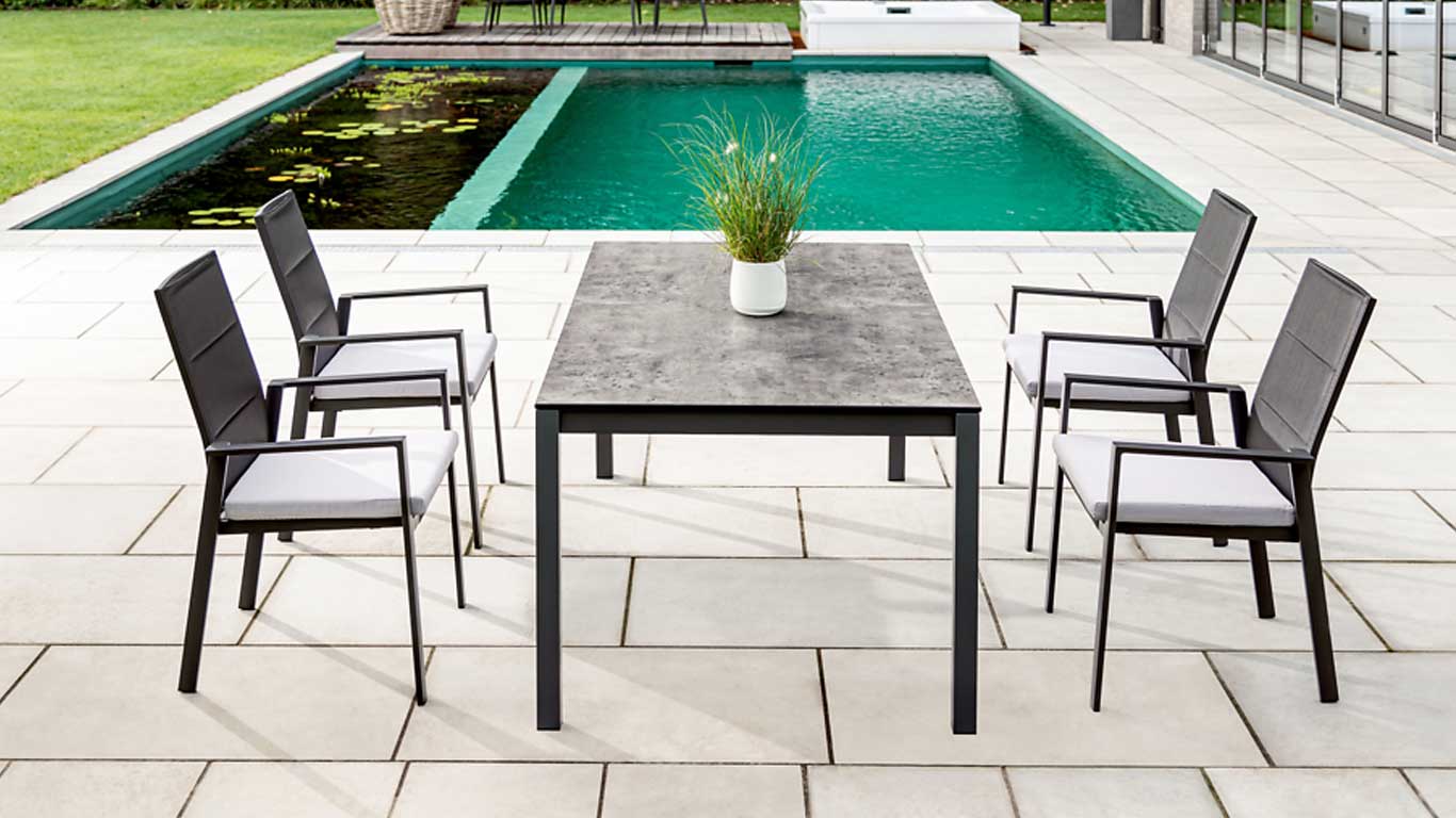 schwarzer Gartentisch mit passenden Gartenstühlen und Polsterung in hellgrau mit Pool und Teich im Hintergrund