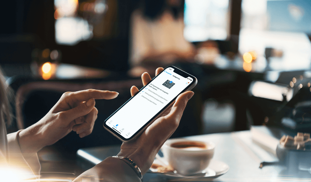 Frau hält Smartphone in der Hand & steuert während des Kaffeetrinkens Ihre Waschmaschine.