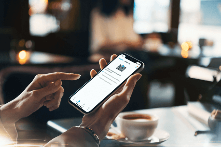 Frau hält Smartphone in der Hand & steuert während des Kaffeetrinkens Ihre Waschmaschine.