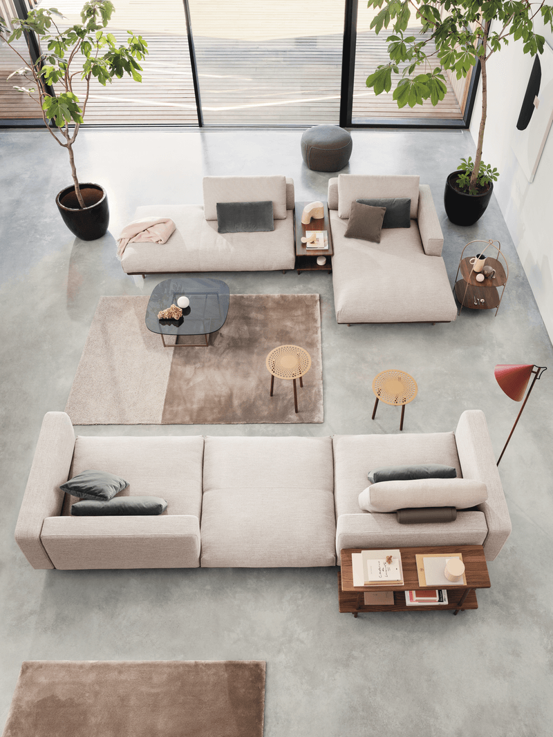 Vogelperspektive auf ein modernes Wohnzimmer mit hellen Sofas, Couchtischen, Teppichen und großen Zimmerpflanzen