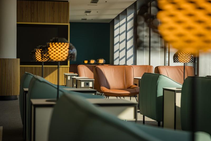 Eine modern eingerichtete Lounge mit bequemen Ledersesseln und stilvollen Lampen in einem lichtdurchfluteten Raum.