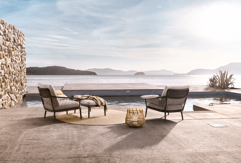 Zwei gemütliche Sessel und ein Tisch auf einer Terrasse mit Blick auf das Meer im Hintergrund