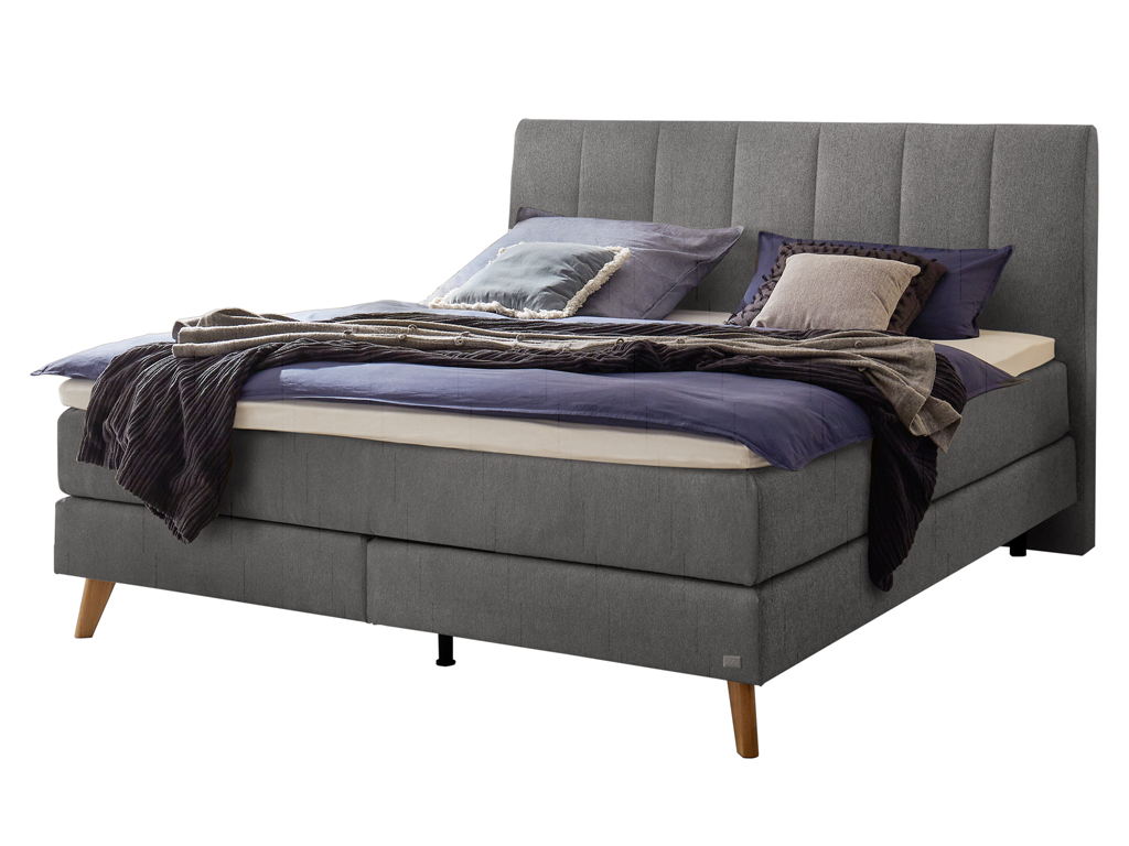 Ein Boxspringbett mit grauen Kopfteil, Holzfüßen und passender Matratze und Bettwäsche vor einem weißen Hintergrund.