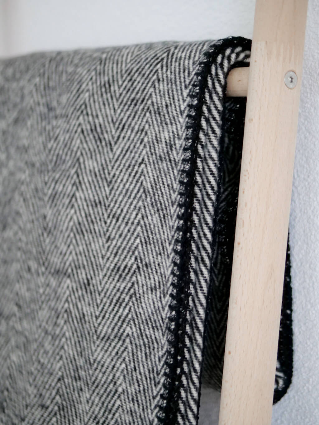 Nahaufnahme einer grauen Woll-Decke mit Fischgrät-Muster, drapiert auf einer Holzleiter.