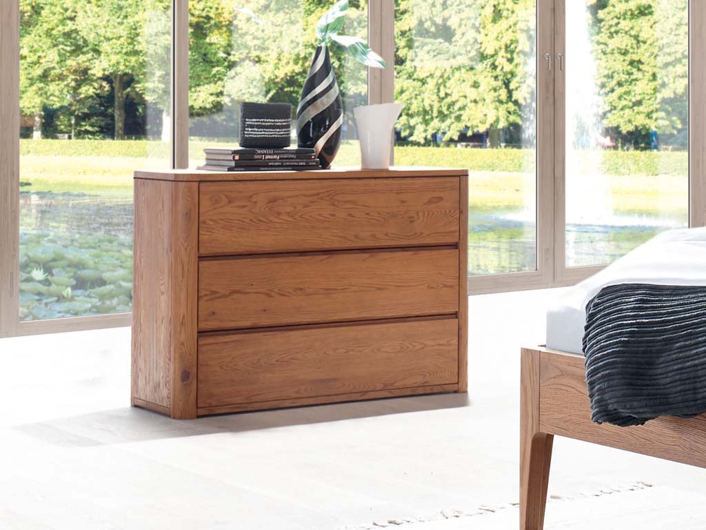 Hasena - Aida Kommode mit 3 Schubladen | Massivholz | B: 105 cm | Eiche massiv konfigurierbar braune Holzkommode mit drei schubladen stilvoll dekoriert in einem hellen raum vor einem großen fenster aida von hasena