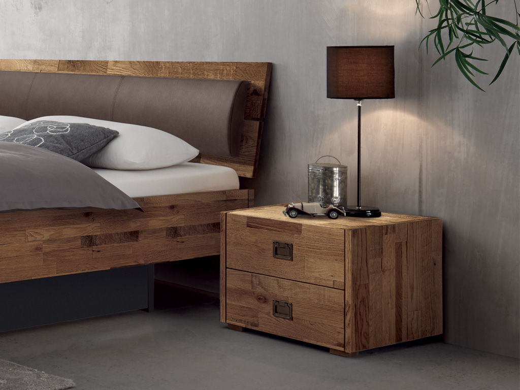 brauner Holznachttisch mit zwei Schubladen und markanten eingelassenen Metallgriffen stehend neber einem Bett stilvoll dekoriert Lica von Hasena
