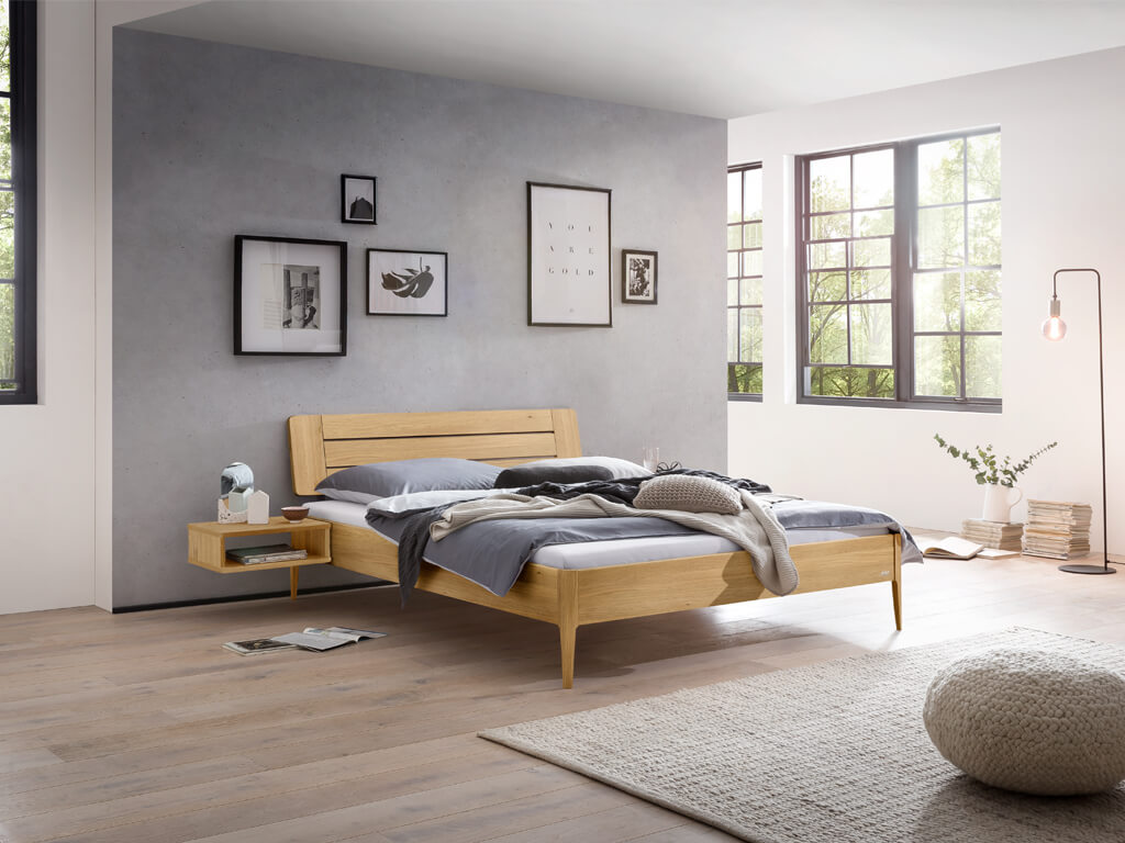 Eine Gesamtaufnahme eines Schlafzimmers mit dem Bettmodell "Busseto" aus heller Eiche. Das Bett ist mit einem am Bett befestigten Nachttisch kombiniert.