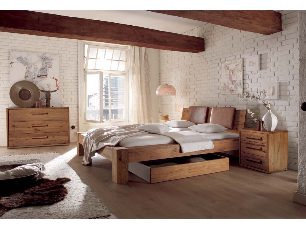 braunes Schlafzimmer in einem gemütlichen Raum mit dicken Balken an der Decke mit einem Bett mit Bettkasten einer Kommode mit drei Schubladen einer kleinen Kommode mit drei Schubladen tilvoll dekoriert Hasena