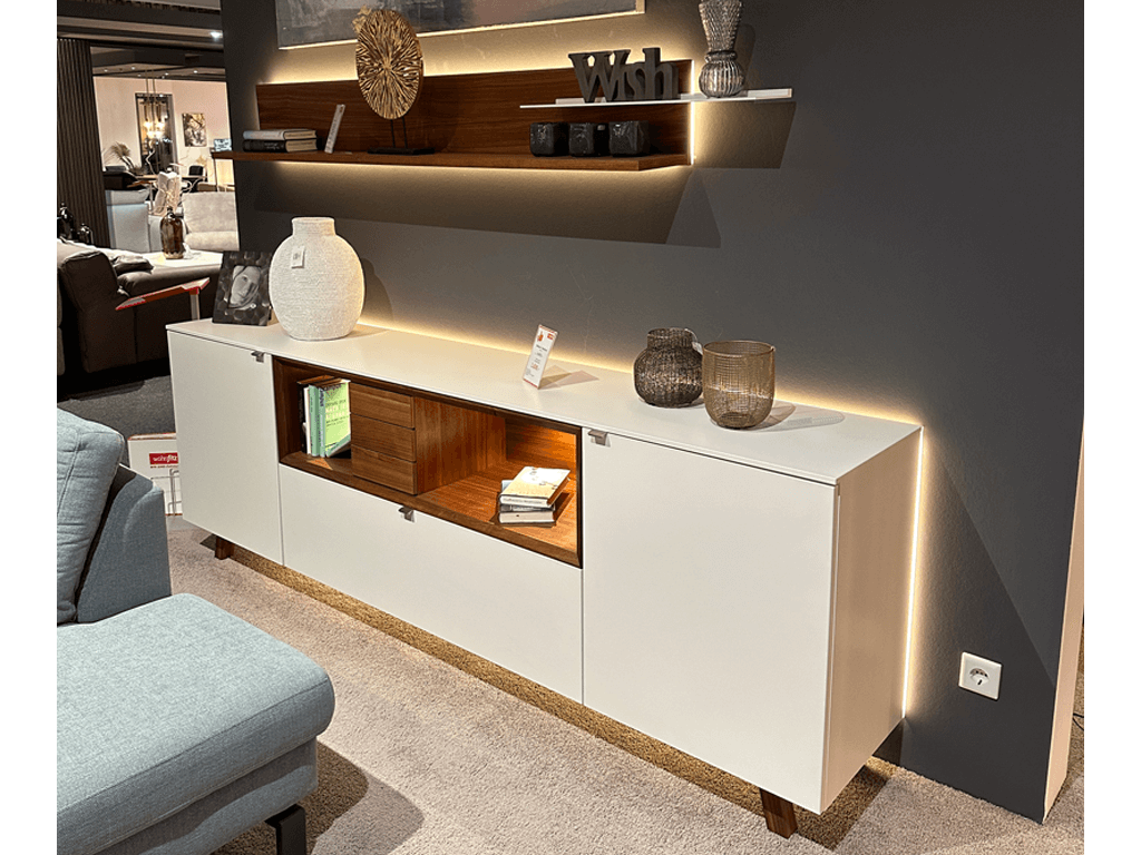 Venjakob ANDIAMO HOME | Sideboard + Wandboard Ein elegantes, modernes Sideboard mit integrierter Beleuchtung, dekoriert mit Vasen und Büchern, in einem stilvoll eingerichteten Wohnzimmer.