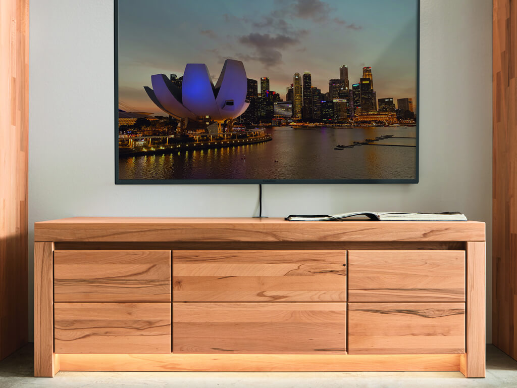 Wöstmann Soleo 3000 - Lowboard | Type 1552 | B: 152,3 cm Eine stilvolle Holzkommode steht vor einer Leinwand, die ein abendliches Stadtpanorama zeigt.