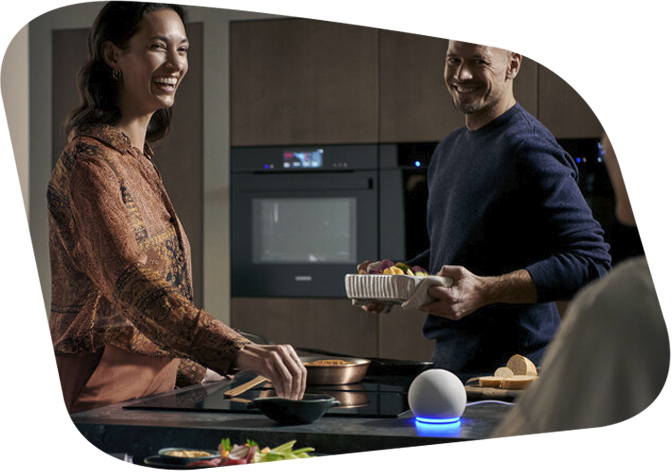 Gruppe von Freunden beim Kochen in einer modernen Küche. Auf dem Tresen steht ein Smart Speaker.