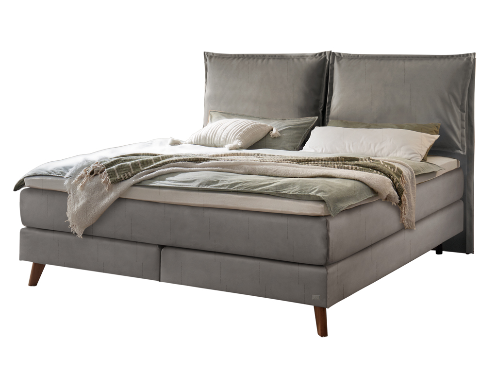 Ein Hasena Boxspringbett Pronto Ricarda mit einem dunklen, stahlgrauen Stoffbezug, das mit Kissen und einer Decke ausgestattet ist.