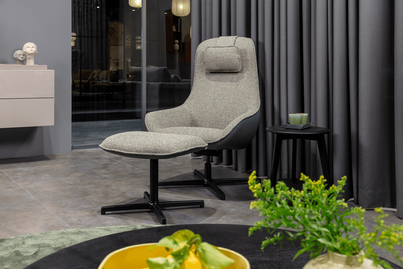 Grauer Loungesessel mit hoher Lehne und Kopfstütze neben einem kleinen Beistelltisch in einem modernen Wohnzimmer