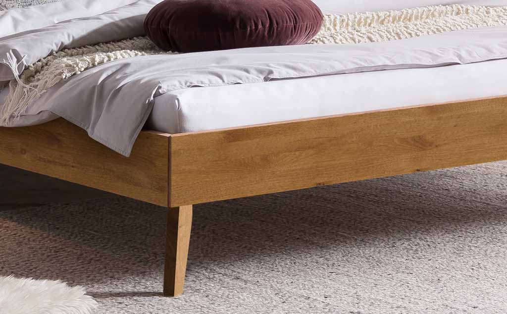 Nahaufnahme eines modernen Bettes aus hellem Holz mit dekorativer Decke und rundem Kissen auf hellem Teppich
